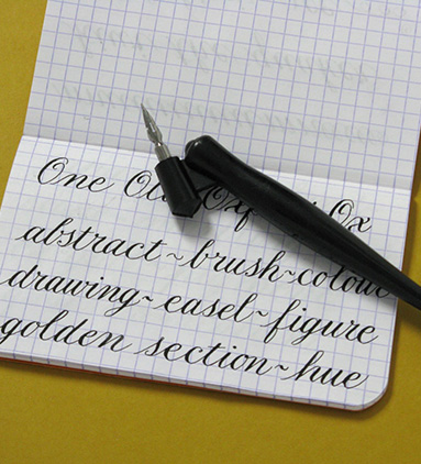 Copperplate calligraphy in small notebook shown with nib and oblique holder